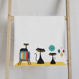 Può includere: Un asciugamano da cucina bianco con un design retrò con tre gatti neri, una televisione vintage e forme geometriche in tonalità di blu, rosso, giallo e verde.