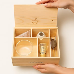 May include: A wooden matcha tea set with a variety of tools, including a whisk, a sifter, a bowl, and a small ceramic cup. The set is presented in a light-colored wooden box with the text "KUMO MATCHA" on the front.