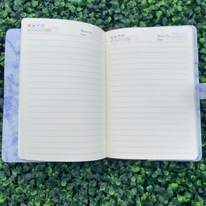 May include: A blue marble-patterned notebook with a white interior and lined pages. The notebook has a brown leather strap and a calendar section on the front cover.