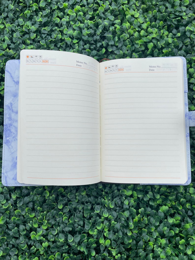 May include: A blue marble-patterned notebook with a white interior and lined pages. The notebook has a brown leather strap and a calendar section on the front cover.
