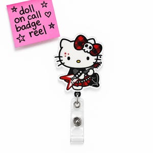 May include: A badge reel featuring a white cat character with a red and black plaid bow, a skull accent, and a red electric guitar. The character wears a black outfit with red accents. A pink note above reads: doll on call badge reel.