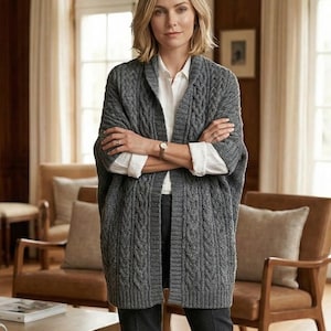 May include: A white ceramic mug with a black handle and the text "But First, Coffee" in a bold, black font. The mug is set against a blurred background, suggesting a cozy setting. The mug appears to be approximately 4 inches tall.