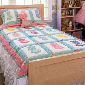 May include: A light wood bed with a matching headboard and footboard. The bed is made up with a quilt and pillow set featuring colorful bonnet designs. The quilt has a white background with blue, pink, yellow, and blue bonnet designs. A pink stuffed doll is on the pillow.