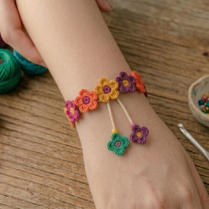 May include: A colorful crochet bracelet featuring vibrant flower designs in shades of orange, purple, yellow, and green. The bracelet is adorned with dangling flower charms. Craft supplies, including yarn and a crochet hook, are visible.