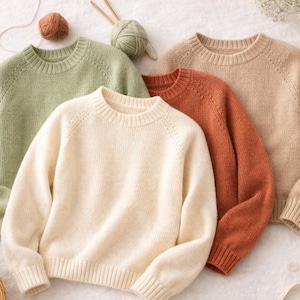 May include: Four crew neck jumpers in soft, muted colours: light green, cream, burnt orange, and beige. The jumpers are made of a knitted material with ribbed cuffs and collars. Yarn and knitting needles are visible in the background, suggesting a handmade or craft theme.