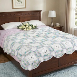 Puede incluir: Una manta de ganchillo blanca y de colores pastel hecha a mano con un borde festoneado se muestra en una estructura de cama de madera oscura. La manta presenta un patrón repetitivo de círculos y cuadrados entrelazados. Almohadas blancas y un ramo de rosas blancas en la cama.