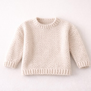 May include: A cream-coloured knitted jumper with a crew neck and long sleeves. The jumper has ribbed cuffs and a ribbed hem. The knit is a chunky, textured stitch, giving it a cosy appearance. The jumper is likely for a child.