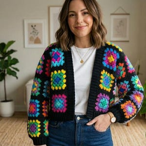 May include: A black crochet cardigan with colorful square patterns. The squares feature a vibrant mix of rainbow colors, including pink, yellow, blue, and green. The cardigan is open-front and appears to be handmade.