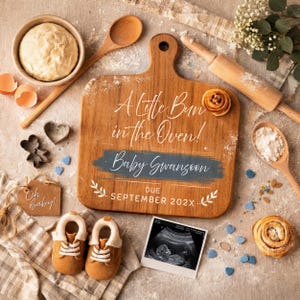 May include: Wooden cutting board with the text "A Little Bun in the Oven!" and "Baby Swanson" with a due date. Includes baby shoes, a sonogram, and baking supplies, announcing a pregnancy.