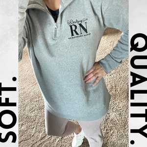 May include: Grey sweatshirt with a black embroidered design that says "Lindsay RN Registered Nurse".