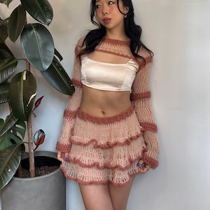 May include: A pink and brown crocheted top and skirt set with a ruffled skirt. The top has a cutout design and the skirt has a layered ruffle design.