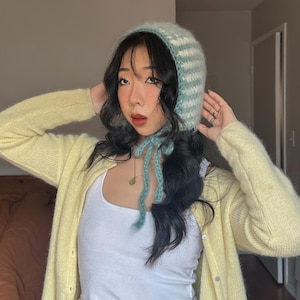 Puede incluir: Un gorro tejido a rayas azules claras y blancas, con cierre de lazo. El conjunto incluye una rebeca amarilla y una camiseta sin mangas blanca. El estilo es suave y c&oacute;modo.
