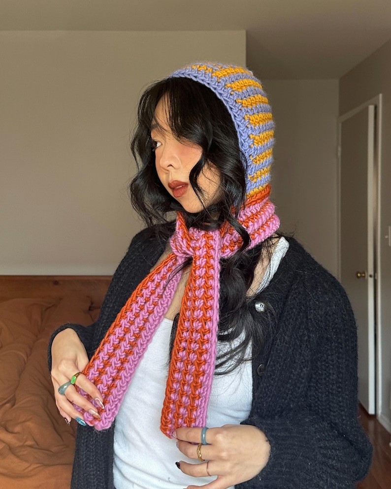 Puede incluir: Conjunto de capucha y bufanda de ganchillo hecho a mano. La capucha es lavanda con rayas amarillas, y la bufanda es rosa y naranja. El conjunto est&aacute; hecho de un hilo suave y texturizado. Un accesorio &uacute;nico y elegante.