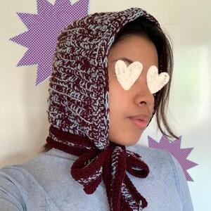 Puede incluir: Un gorro de ganchillo burdeos y azul claro con una corbata a juego. El gorro est&aacute; hecho de un hilo grueso y tiene un aspecto texturizado. La corbata est&aacute; atada con un lazo debajo de la barbilla. El gorro es un art&iacute;culo hecho a mano.
