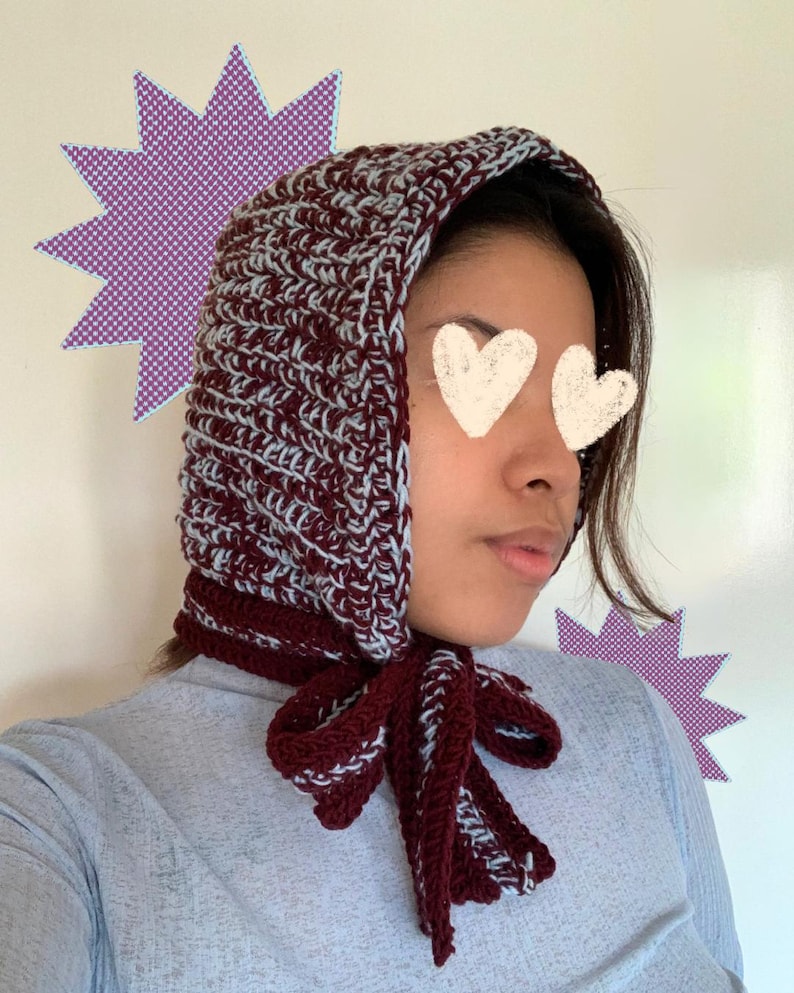 Puede incluir: Un gorro de ganchillo burdeos y azul claro con una corbata a juego. El gorro est&aacute; hecho de un hilo grueso y tiene un aspecto texturizado. La corbata est&aacute; atada con un lazo debajo de la barbilla. El gorro es un art&iacute;culo hecho a mano.