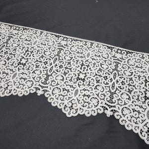 May include: White lace trim with a delicate floral pattern. The lace is intricate and has a scalloped edge.
