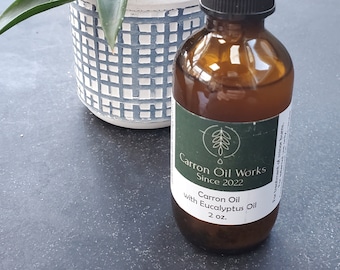 May include: A brown glass bottle with a black dropper top and a green label that reads "Carron Oil Works Since 2022 Carron Oil with Eucalyptus Oil 2 oz."