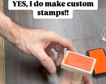 May include: A person's hand holding a wooden stamp with an orange rubber surface. The text "YES, I do make custom stamps!!" is visible in the image.