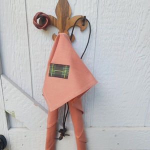 May include: A peach-colored fabric bag with a plaid patch hanging from a wooden hook. The bag is folded and has a brown leather strap.