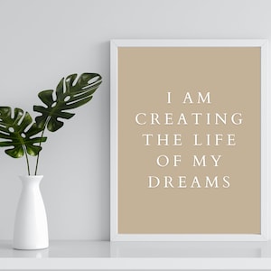 May include: A white framed print with a beige background and the text "I AM CREATING THE LIFE OF MY DREAMS" in white lettering.