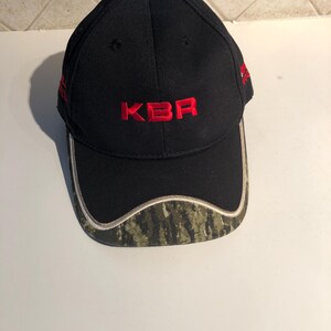 May include: Black baseball cap with a camouflage brim and the red embroidered text "KBR" on the front.