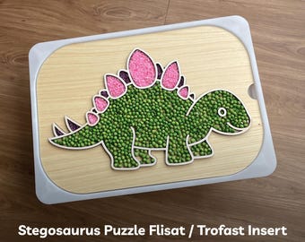 May include: A wooden puzzle insert for a Flisat or Trofast shelf, shaped like a Stegosaurus. The dinosaur is outlined in black and filled with green and pink pea-sized beads. The text "Stegosaurus Puzzle Flisat / Trofast Insert Laser Cut File (SVG, DXF, PDF) ODILIODESIGNS" is printed below the image.