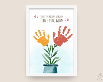 May include: A white framed print with a handprint flower design. The print says "Thanks for helping us bloom I love you, Mom" with two pink hearts on each side of the text.