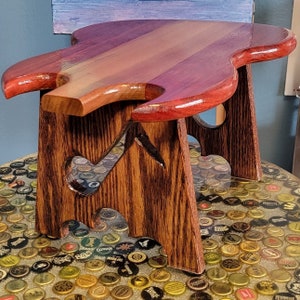 May include: A wooden stool with a unique guitar-shaped top. The top is made of wood with a reddish-brown stain. The stool is made of dark brown wood and has a heart-shaped cutout on each side.