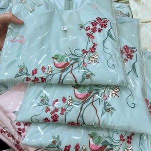 Puede incluir: T&uacute;nica bordada en azul claro con dise&ntilde;o de p&aacute;jaros y flores. La t&uacute;nica est&aacute; empaquetada en pl&aacute;stico transparente. El bordado presenta flores rojas y p&aacute;jaros verdes y rosas. La etiqueta de talla dice XL.