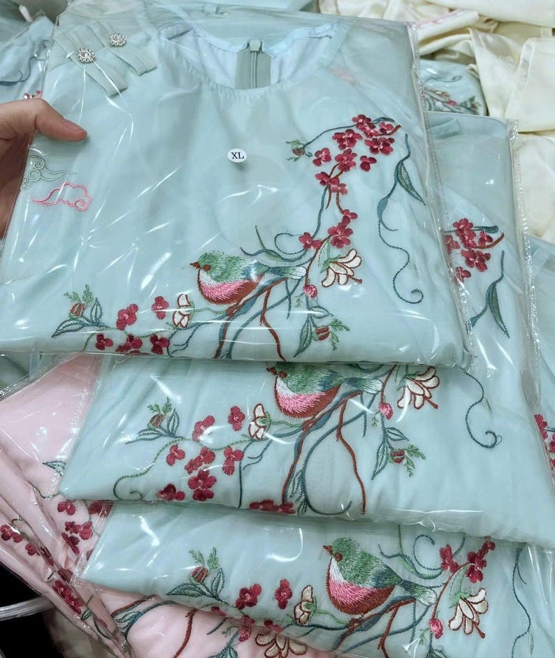 Puede incluir: T&uacute;nica bordada en azul claro con dise&ntilde;o de p&aacute;jaros y flores. La t&uacute;nica est&aacute; empaquetada en pl&aacute;stico transparente. El bordado presenta flores rojas y p&aacute;jaros verdes y rosas. La etiqueta de talla dice XL.