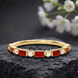 Può includere: Un anello a fascia in oro con un motivo alternato di pietre preziose rosse rettangolari e diamanti bianchi rotondi. L'anello è incastonato con quattro pietre rosse taglio baguette e quattro diamanti rotondi taglio brillante in fila.