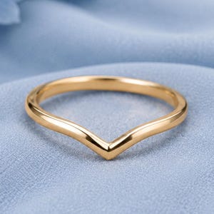 Pode incluir: Um anel de ouro polido com uma banda lisa em forma de V. O anel tem uma construção de metal sólido e contínuo com um perfil arredondado, exibindo um design limpo e simples que termina em ponta no centro da banda.