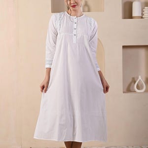 May include: A white cotton nightgown with delicate lace detailing around the neckline and sleeves. The nightgown has a button-up front and a flowing A-line silhouette.