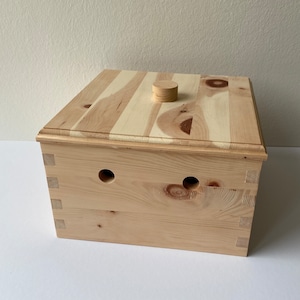 May include: A wooden box with a hinged lid and two holes in the front. The box is made of light wood with a natural finish.
