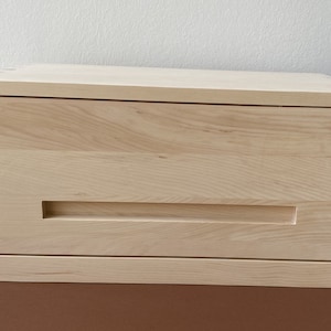 Könnte beinhalten: Eine Schublade aus hellem Holz mit einem einzigen Schubladenzug. Die Schublade ist geschlossen und steht auf einer braunen Oberfläche.