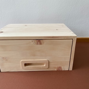 Könnte beinhalten: Ein helles Holzschubladenelement mit einer einzigen Schublade und einem einfachen Holzgriff. Die Schublade ist geschlossen.