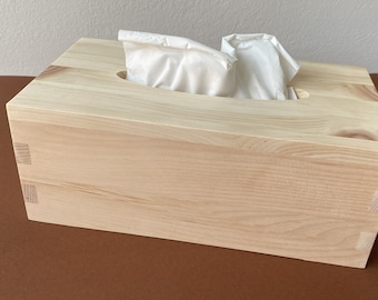 May include: A natural wood tissue box cover with a rectangular shape and a slot for tissues. The box is made of light wood with a smooth finish.