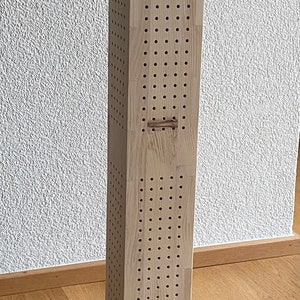 Könnte beinhalten: Ein hoher, rechteckiger Diffusor aus hellem Holz mit quadratischer Basis und einem Muster aus kleinen Löchern auf allen Seiten.