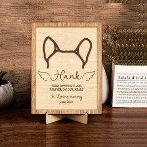 May include: A wooden memorial plaque with a brown dog ear silhouette, the name "Hank", and the text "Your pawprints are forever on our heart. In loving memory. June 2023."