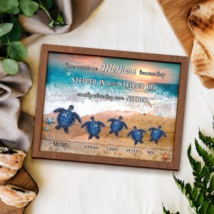 May include: A framed print featuring a beach scene with a sunset, ocean waves, and sand. The print includes five blue sea turtles and the text "Some women are Mothers because they stepped in and stepped up exactly when they were needed."