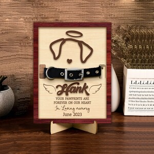 May include: Wooden memorial plaque with a dog silhouette, a black collar, and the name "Hank". The plaque reads "Your pawprints are forever on our heart. In loving memory. June 2023."
