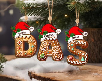 May include: Three personalized Christmas ornaments shaped as the letters D, A, and S. Each gingerbread-style letter is decorated with icing and topped with a Santa hat. The names Diana, Amelia, and Sophie are written on the hats.