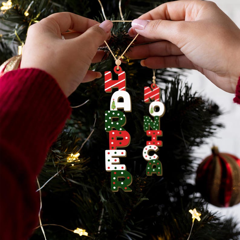 May include: Two personalized Christmas ornaments with the names "Harper" and "Monica" spelled out in vertical letters. The letters are decorated with red and green polka dots, stripes, and Christmas trees.
