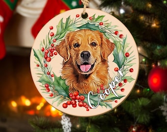 May include: A round Christmas ornament with a watercolor illustration of a golden retriever dog with a red holly wreath and berries. The dog's name, "Cooper", is written in white cursive on the ornament.