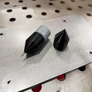 May include: Two black and gray welding torch tips. One tip has the text "428926 30-45 A FineCut Revel" printed on the gray section. The other tip is a solid black cone shape. Both are on a metal surface.
