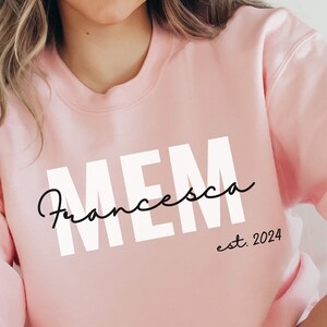 May include: Pink sweatshirt with the text "MEM Francesca est. 2024" in white and black lettering.