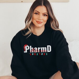 May include: Black sweatshirt with a white "PharmD" graphic and a red Santa hat with a string of colorful lights underneath. The text "Melissa" is written in cursive underneath the "PharmD" graphic.