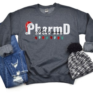 May include: A dark gray sweatshirt with the text "PharmD Melissa" in white with a red Santa hat graphic and a string of colorful Christmas lights.