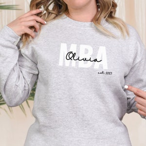 May include: A grey sweatshirt with the text "MBA Olivia est. 2023" printed on the front.