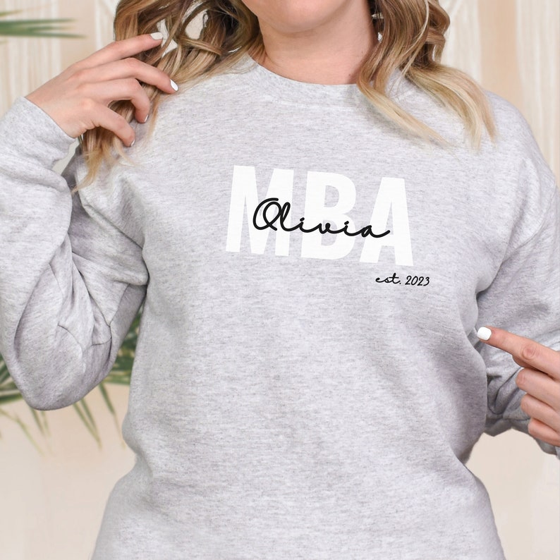 May include: A grey sweatshirt with the text "MBA Olivia est. 2023" printed on the front.